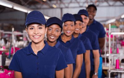 Staff Up America | Top Reasons Milwaukee Employers Rely on Temp Agencies for Fast Hiring Group of diverse workers in blue uniforms and caps smiling in a manufacturing setting, representing staffing solutions and teamwork in Wisconsin's job market.