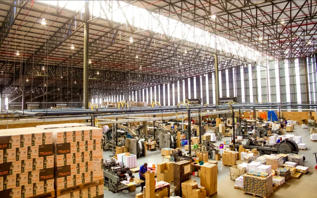 Large industrial warehouse with stacked boxes, machinery, and natural light